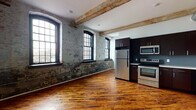 Located at 1821 E Hager St in Philadelphia's vibrant Fishtown neighborhood, this single-floor loft-style unit masterfully blends historic industrial character with contemporary finishes. Throughout the space, rich, warm hardwood floors contrast beautifully with the raw, textured exposed brick walls that speak to the building's storied past. Overhead, original heavy-timber wood beams traverse the ceilings, adding authentic architectural depth and a sense of industrial heritage, while exposed ductwork reinforces the loft aesthetic.

The open living and kitchen area is anchored by a wall of large, black-framed multi-pane windows that flood the interior with natural light and highlight the striking patina of the original masonry. The kitchen is outfitted with dark espresso cabinetry, clean white countertops, and a full suite of stainless steel appliances including a refrigerator, range, built-in microwave, and dishwasher. The bedroom continues the cohesive design language, featuring the same hardwood flooring, an exposed wood beam, and a spacious double-door closet. The overall ambiance is open, airy, and full of character — a seamless fusion of historic industrial design and modern urban living.