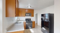 Located in Oakland, CA, this single-story 2-bedroom, 1-bathroom home offers a clean, functional layout with a bright and neutral aesthetic throughout. The living room serves as the welcoming heart of the home, featuring light wood-style flooring, a ceiling fan with light fixture, and a large picture window with vertical blinds that invites generous natural light and outdoor views. The kitchen is well-appointed with warm honey-toned wood cabinetry, light countertops, tile flooring, and black appliances including a gas range, microwave, dishwasher, and refrigerator, along with a stainless steel sink positioned beneath a window. Both bedrooms are carpeted and finished with crisp white walls, offering a comfortable and calm atmosphere. The bedrooms are served by a central hallway and benefit from windows that allow natural light to filter in. The full bathroom is neatly finished in white with tile flooring, a shower-tub combination, and a small window for ventilation. Throughout the home, clean white walls, consistent flooring choices, and ceiling fans contribute to a cohesive, move-in-ready feel that maximizes the efficiency of the well-organized floor plan.