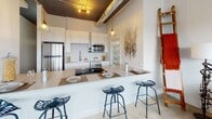 Located at 206 North Ave in Webster, NY, this loft-style unit blends industrial character with modern comfort in a distinctive and thoughtfully designed layout. The open-concept kitchen anchors the living space, featuring white shaker cabinetry, stainless steel appliances including a refrigerator, microwave, and electric range, and a generous peninsula with bar seating for three. Exposed ductwork and pendant lighting hang from the soaring dark-painted ceiling, adding an authentic industrial aesthetic throughout.

The living area is generously proportioned, accommodating dual sofas arranged around a patterned area rug. Large multi-pane windows with roller shades flood the space with natural light and offer sweeping views of the surrounding landscape, creating an airy, elevated ambiance.

The bedroom features a striking structural column, dark ceiling treatment, and carpeted flooring, lending it a cozy yet architecturally interesting character. A walk-in closet is accessible from within the bedroom, providing ample storage.

The full bathroom is clean and functional, finished in crisp white tones with a double-sink vanity, a shower with glass door, and a separate tub-shower combination. The polished concrete-style flooring runs throughout the main living areas, tying the industrial design language together cohesively.