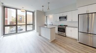 This well-appointed single-floor space showcases a thoughtfully designed open-concept layout with a seamless flow between the living and kitchen areas. Light-toned hardwood flooring runs throughout, lending warmth and continuity to the interior.

The kitchen is a standout feature, outfitted with crisp white cabinetry, sleek gray countertops, and a full suite of stainless steel appliances including a gas range, built-in microwave, dishwasher, and refrigerator. A center island provides additional prep and gathering space, while stylish pendant lighting and a classic white subway tile backsplash add refined finishing touches. Floor-to-ceiling windows along one wall flood the kitchen and living area with abundant natural light and offer views of the surrounding neighborhood, creating an airy and open atmosphere.

The living area is generously proportioned, with neutral walls, recessed lighting, and clean architectural lines that give the space a modern, move-in-ready character.

The bathroom is finished with large-format floor tiles, a gray vanity with a white countertop and undermount sink, a tiled walk-in shower with decorative mosaic accents, and a well-placed mirror. Together, every area of this space reflects a consistent commitment to contemporary design and quality finishes.