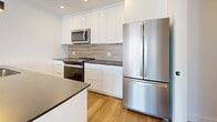 Located at 6450 Bayers Road in Halifax, Nova Scotia, this well-appointed 2-bedroom, 2-bathroom residence offers a clean, modern aesthetic throughout its generously sized single-floor layout. Light hardwood flooring flows seamlessly through every room, complemented by crisp white walls, recessed lighting, and bold matte black door hardware that adds a contemporary contrast.

The open-concept kitchen and living area serves as the heart of the home. The kitchen is outfitted with sleek white cabinetry extending to the ceiling, dark countertops, a wood-toned tile backsplash, and a full suite of stainless steel appliances including a French door refrigerator, electric range, built-in microwave, and dishwasher. The living room benefits from large windows that bring in an abundance of natural light, with baseboard heating and a wall-mounted mini-split unit providing year-round climate control.

The hallway connects two well-sized bedrooms, both bright and neutrally finished. The primary bedroom offers a comfortable footprint with a window view. Both bathrooms are finished in a minimalist style, featuring white surrounds, soaker tubs, dark-topped vanities, and wood-look flooring. A dedicated laundry area houses a stacked Whirlpool washer and dryer, adding everyday convenience to this thoughtfully designed residence.