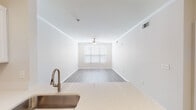 Located at 4209 Lassiter Mill Rd in Raleigh, NC, this single-floor residence offers a clean, modern design with a cohesive neutral palette throughout. The open-concept layout connects the kitchen and living areas seamlessly, creating a spacious and functional flow. The kitchen is outfitted with crisp white shaker-style cabinetry, quartz countertops, a classic white subway tile backsplash, and stainless steel appliances including a refrigerator, electric range, and built-in microwave. A peninsula with an integrated sink serves as a natural divide between the kitchen and the adjacent living space. The living area features light wood-look flooring, crown molding, and a ceiling fan, with a window providing natural light. A separate room with French doors and a transom window above offers additional flexible living space, also accented by a ceiling fan and matching flooring. The bedroom includes a walk-in closet with built-in shelving and rod storage, along with access to a hallway leading to additional spaces. The bathroom is finished with wood-look flooring, a tub-shower combination with tile surround, and clean, simple fixtures. Throughout the unit, consistent finishes—crown molding, neutral tones, and wood-look floors—contribute to a cohesive and well-appointed interior.