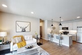 Located at 2000 Swenson Ln in Saint Peters, MO, this thoughtfully designed one-bedroom, one-bathroom residence offers a smart, efficient layout across a single floor. The open-concept living and kitchen area creates a seamless flow, anchored by warm wood-look flooring that extends throughout the home. The living room is bright and welcoming, benefiting from a large sliding glass door that floods the space with natural light and provides direct outdoor views. The kitchen is a standout feature, boasting white shaker cabinetry reaching to the ceiling, sleek white quartz countertops, a peninsula with bar seating, stainless steel appliances including a refrigerator, electric range, and built-in microwave, all accented by stylish black pendant lighting. The generously sized bedroom offers a ceiling fan, ample natural light, and direct access to a dedicated walk-in closet with built-in shelving and hanging rods. The bathroom features a full tub and shower combination with classic white subway tile surround and chrome fixtures. A hallway connects all areas efficiently, completing this well-planned residence ideal for comfortable single-occupant or couple living in Saint Peters.
