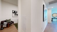Located on the 21st floor of a contemporary high-rise on Wilshire Boulevard in Los Angeles, this well-appointed residence offers a refined urban living experience with sweeping panoramic views of the city skyline and the San Gabriel Mountains. Floor-to-ceiling glass windows flood the interior with abundant natural light, while the open-plan living area showcases light hardwood flooring and a clean, modern aesthetic. The living room is anchored by a dramatic wall of glass that frames unobstructed cityscape views and provides direct access to a generous private balcony enclosed by sleek glass railings—ideal for enjoying the Los Angeles skyline. The kitchen features flat-front white cabinetry extending to the ceiling, stainless steel appliances including a range, microwave, dishwasher, and refrigerator, complemented by a glass tile backsplash and light countertops. The bedroom benefits from its own floor-to-ceiling windows with stunning mountain and city views. A spacious walk-in closet with built-in shelving and hanging rails provides ample storage. The bathroom is finished with large-format stone-look tiles, a floating vanity with illuminated mirror, a glass-enclosed shower, and a soaking tub. A dedicated office nook completes this thoughtfully designed urban retreat.