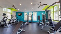 Located at 5550 Bexley Way NW in Concord, NC, this fitness center is a thoughtfully designed, single-floor facility built to support a comprehensive workout experience. The space is immediately distinguished by its bold interior palette — vivid teal accent walls and lime green trim frame the room, creating an energetic and motivating atmosphere. Recessed lighting and ceiling fans are distributed throughout, ensuring the space remains well-lit and comfortable during any workout.

The facility is divided into clearly defined zones. A dedicated cardio area features a row of treadmills positioned beneath soaring vaulted ceilings and large multi-pane windows that flood the space with natural light and views of the surrounding greenery. Adjacent to this, elliptical trainers and stationary bikes provide additional low-impact cardio options.

The strength training section is generously outfitted with cable machines, a squat rack, and multiple adjustable benches for free weight exercises. A full dumbbell rack stocked with a wide range of weights caters to all fitness levels. Floor-to-ceiling mirrors line one wall, enhancing the sense of openness while allowing users to monitor their form. The durable rubber flooring throughout provides both safety and sound absorption. A wall-mounted television adds an entertainment element, rounding out this fully appointed fitness facility.