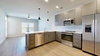 This 1-bedroom, 1-bathroom residence is thoughtfully laid out across a single floor, offering a clean and modern living experience. The open-concept kitchen is a standout feature, outfitted with sleek gray cabinetry extending to the ceiling, white quartz countertops, a subway tile backsplash, and a full suite of stainless steel appliances including a side-by-side refrigerator with ice maker, electric range, built-in microwave, and dishwasher. Stylish pendant lighting accents the kitchen peninsula, which flows naturally into the living area. The living room is bright and welcoming, featuring light wood-look flooring, neutral walls, and a glass-paneled door that invites natural light and provides outdoor access. The generously sized primary bedroom is finished with plush carpeting, soft neutral tones, a ceiling fan, and a sizable window with blinds that fills the room with daylight. A dedicated closet provides ample storage. Throughout the unit, clean white trim, recessed lighting, and a consistent neutral color palette create a cohesive, contemporary ambiance suited for comfortable everyday living.