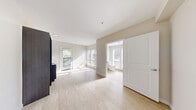 Located at 8500 20th Ave NE in Seattle's Ravenna neighborhood, this efficiently designed single-floor studio offers a bright and contemporary living environment. Light wood-look flooring runs throughout, complementing the clean, neutral wall tones that give the space an airy, open feel.

The main living area benefits from generous natural light streaming through multiple windows and a glass-panel door that opens to a private balcony, offering pleasant outdoor views of surrounding greenery. The open layout makes excellent use of the available footprint, with a dedicated open-concept closet unit featuring dual hanging rods providing organized storage without enclosing the space.

The kitchenette is integrated seamlessly along one wall, showcasing dark-toned cabinetry with a modern finish, stainless steel hardware, and a sink — delivering a sleek, functional cooking area. Recessed lighting adds to the contemporary aesthetic.

The bathroom is thoughtfully designed with accessibility in mind, equipped with a walk-in shower featuring stainless steel grab bars for added safety and support, alongside a window that introduces natural light. The space is clean and functional, with a bright white finish throughout.

Overall, this studio presents a well-considered, modern design that maximizes comfort and usability, making it a practical and stylish option in the heart of Seattle.