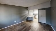 Located at 7250 Campbellton Rd SW in Atlanta, GA, this efficiently designed single-floor unit offers a practical and cohesive layout across its living area, kitchenette, and bathroom. The living space is finished with rich wood-look vinyl plank flooring and cool-toned gray walls accented by crisp white baseboards and trim, creating a clean, modern aesthetic. A window with blinds allows natural light to filter in, offering a view of the surrounding greenery outside. A wall-mounted HVAC unit ensures year-round climate control. The open kitchenette flows naturally from the living area, featuring white cabinetry, a granite-style countertop, a sink, and a tile backsplash. A pass-through shelf connects the kitchen to the main living space, enhancing the sense of openness. A sliding door provides access to additional storage. The bathroom is neatly appointed with wood-look flooring consistent with the rest of the unit, a vanity with a granite-style countertop, and light gray walls. A textured ceiling is present throughout the unit, adding a subtle design detail. The overall layout is thoughtfully organized, making efficient use of every square foot while maintaining a cohesive and contemporary interior style.