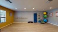 Located at 1300 Southampton Rd in Benicia, CA, this single-floor fitness studio is purpose-built for group or individual exercise. The space features light hardwood-style flooring throughout, providing a clean, durable surface ideal for a wide range of physical activities. Recessed lighting illuminates the interior evenly, complementing the natural light that filters in through multiple louvered windows fitted with plantation shutters.

The studio is divided into distinct functional zones. One area features a wall-mounted ballet barre and a vibration platform, set against a striking yellow accent wall and gray backdrop—ideal for barre classes, stretching, or balance training. An organized equipment rack holds exercise mats, medicine balls, resistance bands, and stability balls, keeping the space tidy and accessible.

An adjacent area showcases a full wall of floor-to-ceiling mirrors paired with a wall-mounted flat-screen TV, perfect for guided workouts or instructor-led classes. A rolling dumbbell rack stocked with color-coded free weights provides convenient access to strength training tools.

French doors with glass panes connect the two sections of the studio, adding architectural character while maintaining an open, airy feel. Motivational fitness charts and instructional posters are displayed throughout, reinforcing the space's professional, activity-focused atmosphere.
