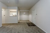 Located at 3601 Clinton Pkwy in Lawrence, Kansas, this single-floor unit offers a practical and comfortable layout designed for everyday living. The open living and dining area is finished with neutral-toned carpet, a ceiling fan with light fixture, and a pass-through window connecting to the kitchen, which enhances the sense of openness. A pendant light over the dining area adds a subtle design accent. The front of the unit features a door with adjacent windows that allow natural light to fill the space and provide views of the surrounding greenery. The galley-style kitchen is outfitted with white cabinetry, light countertops, and white appliances including a refrigerator, electric range, microwave, and dishwasher, all set over wood-look plank flooring. A louvered door leads to additional storage within the kitchen. The bedroom is generously proportioned with carpeted flooring, a ceiling fan, dual windows overlooking the outdoors, and a reach-in closet with built-in shelving. The bathroom features a single-sink vanity with a wide mirror, wood-look tile flooring, and a tub-shower combination enclosed by sliding glass doors. Throughout the unit, neutral wall tones and consistent finishes create a cohesive and functional living environment.