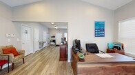 Located at 1600 Brooks Pointe Cir in Travelers Rest, SC, this single-floor professional office suite offers a well-organized and inviting layout ideal for client-facing operations. The space is entered through glass double doors that flood the entry with natural light and offer views of the surrounding greenery, creating an immediately welcoming first impression.

Just inside, a reception area features a warm wood-toned front desk, vaulted ceilings with recessed lighting, and a small seating arrangement with upholstered chairs — providing a comfortable waiting area for visitors. Light gray walls and durable wood-look luxury vinyl plank flooring run throughout, lending a clean, cohesive aesthetic.

A private office is situated toward the rear, equipped with a large executive desk, guest seating, and a wall-mounted monitor, with a bright window offering natural light. Adjacent to the main area, a functional kitchenette includes gray cabinetry, a full-size refrigerator, microwave, and ample counter space for staff convenience.

Additional amenities include a water fountain, restroom access, and a printer/copier station. The space is practical, professionally appointed, and move-in ready for a variety of business uses.