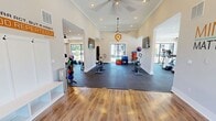 Located at 8000 Revolution Way in Covington, GA, this 1,510-square-foot fitness center at Pointe Grand spans a single floor and is designed to support a well-rounded workout experience. The facility is divided into two functional zones, each thoughtfully appointed for different training styles.

The welcoming entryway features warm hardwood-style flooring, built-in storage cubbies, and a branded welcome mat, setting an energetic tone from the moment you walk through the glass double doors. High ceilings with crown molding carry throughout the space, lending an open and airy atmosphere.

The cardio area is outfitted with air bikes, stationary cycles, and elliptical machines, all positioned on durable rubber flooring. Ceiling fans and wall-mounted flat-screen TVs enhance comfort during workouts, while large windows and glass doors flood the room with natural light and offer views of the surrounding community.

The strength training zone is equally well-equipped, featuring a bold yellow power rack with Olympic barbells, a dumbbell rack, a punching bag, and plyo boxes. Motivational quotes and branded graphics — including a Wayne Gretzky quote and a "Mind Over Matter" display — are painted directly onto the walls, reinforcing an atmosphere of determination and focus. Recessed lighting and ceiling fans complete the space, ensuring a comfortable and inspiring environment for all fitness levels.
