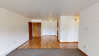 This single-floor unit offers a practical and comfortable layout with a mix of warm hardwood-style flooring and plush carpeting throughout. The living area is bright and open, featuring a sliding glass door that floods the space with natural light and provides views of the surrounding greenery outside. A wall-mounted air conditioning unit and baseboard heating ensure year-round comfort. A ceiling fan adds to the functionality of the connected interior space.

The galley-style kitchen is efficiently designed with warm oak cabinetry featuring gold hardware, ample upper and lower cabinet storage, a double-basin stainless steel sink, and white appliances including a coil-top range and a full-size refrigerator. The hardwood-style flooring continues seamlessly through the kitchen, adding a cohesive feel.

The bedroom is carpeted and features a generously sized closet with sliding doors, built-in shelving, and a hanging rod for storage. A wood-trimmed window allows natural light to filter in while maintaining privacy. The entry area includes warm-toned wood interior doors and connects the various spaces of the unit in a straightforward, accessible flow. Clean white walls throughout keep the overall ambiance bright and neutral, offering a versatile canvas for personalization.