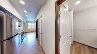 This single-floor unit offers a thoughtfully arranged layout that balances functionality with modern design. Throughout the space, warm wood-tone luxury vinyl plank flooring and crisp white walls create a clean, welcoming aesthetic complemented by rich dark wood trim and door frames.

The kitchen is a standout feature, outfitted with rich dark-stained cabinetry, stainless steel appliances including a range, microwave, and dishwasher, and a countertop with a tile backsplash. The kitchen opens to the living area, promoting a connected, open feel.

A central hallway serves as the spine of the unit, providing access to the various rooms. Notable details include a stylish sliding barn door, recessed lighting, and vaulted ceiling elements that lend a sense of height and openness to the corridor.

The bathroom is finished with matching wood-toned cabinetry, a single vanity with a stone-topped sink, a large mirror with overhead lighting, and coordinating hardware throughout. Wood-look flooring continues into this space, maintaining design consistency.

The bedroom is bright and airy, featuring a large bank of windows that invite abundant natural light and offer views of the surrounding neighborhood. The room provides ample wall space and a neutral palette, making it highly adaptable. Overall, the unit presents a modern, move-in-ready living environment with cohesive finishes throughout.