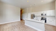 Located at 1105 Blaine Ave in Indianapolis, Indiana, this thoughtfully designed 1-bedroom, 1-bathroom home offers a clean, modern aesthetic throughout its single-floor layout. The open-concept kitchen and living area serves as the heart of the home, featuring light wood-look flooring, soaring ceilings with recessed lighting, and abundant natural light streaming through multiple windows. The kitchen is well-appointed with crisp white shaker-style cabinetry, stainless steel appliances including a refrigerator, range, and microwave, and a large central island with a white quartz countertop and double stainless steel sink — ideal for both cooking and casual dining. The spacious bedroom is carpeted for comfort and includes a natural light-filled window with outdoor views. Three closets provide generous storage, including a walk-in closet with wire shelving. The full bathroom features a tiled tub/shower combo, white vanity cabinetry, and wood-look flooring. A dedicated laundry area, utility room, and hallway with additional closet space round out the practical layout. Neutral warm-toned walls and consistent modern finishes throughout lend the home a cohesive, move-in ready feel.