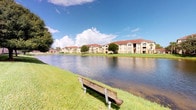 This single-floor residence is situated within a multi-building residential community that showcases classic Florida Mediterranean-style architecture, characterized by warm stucco exteriors and terracotta-toned rooflines. The community's most notable outdoor feature is a expansive pond that serves as a central focal point, with well-manicured grass banks lining its edges and a wooden bench positioned along the waterfront, offering a tranquil spot to enjoy the open water views and the broad, sun-filled sky above.

The grounds are thoughtfully landscaped with mature trees and neatly trimmed lawns that contribute to a serene, resort-like ambiance. The buildings surrounding the pond are multi-story, suggesting a sizeable community with a variety of unit configurations. The outdoor common areas appear spacious and well-maintained, providing residents with pleasant green space to enjoy.

Unfortunately, the interior images provided are too underexposed to reveal meaningful detail about the unit's rooms, finishes, or layout. Based on available information, the residence occupies a single floor, offering straightforward, accessible living without the need for stairs. The overall setting of the community suggests a comfortable and peaceful living environment with appealing waterfront scenery.