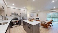 Located at 8003 NE 13th Ave in Vancouver, WA, this thoughtfully designed 2-bedroom, 2-bathroom single-floor residence offers a clean, contemporary aesthetic throughout. The open-concept kitchen and living area serves as the heart of the home, featuring a two-tone kitchen with light upper cabinetry, dark lower cabinets, white quartz countertops, a classic subway tile backsplash, and a full suite of stainless steel appliances. A central island with bar seating provides additional prep space and casual dining. The living area flows naturally from the kitchen and is highlighted by a sleek wall-mounted electric fireplace and light-toned luxury vinyl plank flooring that runs throughout the home. A sliding glass door opens to a private balcony with views of surrounding greenery. Both bedrooms are bright and comfortable, each receiving natural light through large windows. The primary bedroom includes its own dedicated space, while the second bedroom features a wall-mounted mini-split system for personalized climate control. The bathrooms are finished in neutral tile with modern dark-hardware vanities. Additional conveniences include in-unit laundry, a pantry, three closets, and a hallway connecting the living and sleeping areas seamlessly.