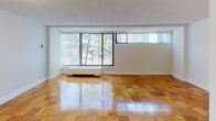 This single-floor residence offers a thoughtfully laid-out living space that combines classic design elements with functional comfort. The main living area is a standout feature, showcasing gleaming parquet hardwood flooring in a warm honey tone that extends throughout the unit. Large windows fitted with vertical blinds flood the room with natural light and offer pleasant views of surrounding greenery, creating a bright and airy atmosphere. A baseboard heating unit runs beneath the windows, ensuring year-round comfort.

The kitchen is efficiently designed with warm oak cabinetry offering ample upper and lower storage, a stainless steel sink, light countertops, and white appliances including a full-sized refrigerator. The tile flooring in this area provides a clean contrast to the hardwood found in the rest of the unit.

The bedroom continues the parquet hardwood flooring and features a built-in closet with shelving, providing generous storage solutions. The room benefits from the same clean, neutral wall tones found throughout the space, contributing to a cohesive and calming aesthetic.

The bathroom is finished in crisp white, featuring a full-sized soaking tub with an overhead shower, white tile surround, and chrome fixtures, delivering a clean and classic look. Overall, the space presents a well-maintained, functional residence with timeless finishes.