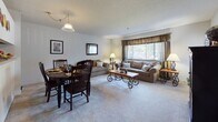 Located in the Normandy community of New Britain, CT, this single-floor residence offers a well-organized and functional layout. The open-concept living and dining area is generously proportioned, featuring soft wall-to-wall carpeting, a pendant light over the dining space, and large windows dressed with decorative curtains that invite natural light. The living area accommodates a full sofa arrangement centered around a decorative wood and iron coffee table, creating a welcoming gathering space. The kitchen runs along a galley-style configuration, lined with warm oak cabinetry, ample counter space, and includes white appliances such as an electric range, dishwasher, and refrigerator. The layout allows for easy flow between the kitchen and main living areas. The bedroom is a comfortable retreat with plush carpeting, a generous closet with wooden bi-fold doors, and a sliding glass door draped with floor-length curtains that allow for natural light. The full bathroom features a tub-shower combination, neutral tile flooring, and clean white fixtures, providing a practical and tidy space. Throughout the residence, neutral tones, textured ceilings, and consistent finishes contribute to a cohesive and understated aesthetic.