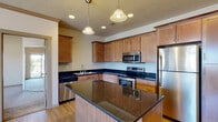 This single-story unit at 121 East Victory Road in Meridian, Idaho offers a functional and cohesive layout designed for comfortable everyday living. The kitchen serves as a central highlight, featuring rich warm-toned cabinetry that extends to the ceiling for generous storage capacity. Dark granite countertops run throughout, including across a spacious central island that provides additional prep space and seating potential. A full suite of stainless steel appliances—including a refrigerator, electric range, over-the-range microwave, and dishwasher—completes the kitchen. Pendant lighting and recessed fixtures illuminate the space effectively. Light hardwood-style flooring flows through the kitchen and connecting areas, contributing to a clean, cohesive aesthetic. The living areas are finished with neutral-toned carpet and feature crown molding details, textured ceilings, and windows that allow natural light to enter. A bathroom includes a wood-toned vanity with dark granite countertop, a large mirror, and a shower-tub combination. Additional bedrooms offer carpeted flooring in a quiet, understated palette. A dedicated laundry room with full-size washer and dryer hookups adds everyday convenience to this well-organized Meridian residence.