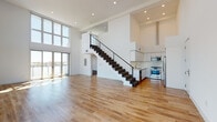 Located at 901 Vine St in the heart of Los Angeles, this modern two-story residence showcases a striking open-concept design anchored by a dramatic double-height main living area. Expansive floor-to-ceiling windows flood the space with abundant natural light while offering sweeping city views, and warm hardwood floors run throughout the main level, enhancing the airy, loft-like atmosphere.

A sleek staircase with a dark metal cable railing serves as a central architectural focal point, connecting the two floors with contemporary elegance. The kitchen is outfitted with crisp white flat-panel cabinetry, a white tile backsplash, stone countertops, and stainless steel appliances, including a gas range and built-in microwave.

The upper level features carpeted bedrooms bathed in natural light. One bedroom opens directly onto a private balcony through a full-height sliding glass door, offering open views of the Los Angeles skyline. Additional windows on the upper level overlook the double-height living area below, reinforcing the sense of openness throughout.

The bathrooms are finished with mosaic tile flooring, white vanities, and marble-style tiled tub surrounds, providing a clean, refined aesthetic. Additional storage is available under the staircase on the main level, adding practical functionality to this well-designed urban residence.