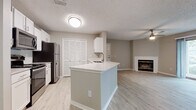 This renovated apartment showcases a thoughtful blend of style and functionality. The open-concept living area boasts a sleek kitchen with white cabinetry, stainless steel appliances, and a convenient island. The adjacent living room features a cozy fireplace and sliding glass doors leading to outdoor space. Light wood-look flooring unifies the space, complemented by neutral walls. Two updated bathrooms offer modern fixtures and finishes. Ample natural light floods through large windows, while ceiling fans provide comfort. A walk-in closet offers generous storage. The overall design creates an inviting, contemporary living environment.