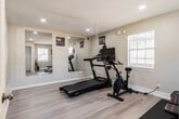 Located at 2700 Temple Crest Dr in Birmingham, Alabama, this dedicated fitness center offers a well-organized exercise space designed to support a complete workout routine. The room features light-toned luxury vinyl plank flooring that lends a clean, modern aesthetic throughout, complemented by neutral beige walls and a textured ceiling with recessed lighting that keeps the space bright and inviting.

Large wall-mounted mirrors are strategically placed to visually expand the room and allow users to monitor their form during exercise. Multiple windows with white louvered blinds allow natural light to filter in, enhancing the open, airy feel of the space. Safety equipment, including fire extinguishers, is visibly mounted on the walls.

The exercise room is equipped with a treadmill, a stationary spin bike with an integrated display monitor, a multi-position adjustable workout bench, a dumbbell set, and additional cardio and strength training accessories. A dedicated entry door provides easy, direct access to the facility.

Motivational fitness artwork adorns the walls, contributing to an energetic and purpose-driven atmosphere. The layout is thoughtfully arranged to maximize usability within the space, making this fitness center a practical and functional amenity for residents at 2700 Temple Crest Dr.