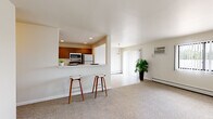 This single-floor residence offers a thoughtfully arranged layout that balances open communal spaces with private rooms. The heart of the unit is an open-concept kitchen and living area, where a peninsula countertop with seating for two bar stools serves as a natural divider. The kitchen is equipped with stainless steel appliances, including a microwave and refrigerator, and features warm wood-toned cabinetry. A separate, updated kitchen area showcases contemporary gray cabinetry, light marble-style countertops, hardwood-style flooring, and a full suite of appliances including a dishwasher and range.

The living area is generously sized, finished with neutral carpet, and receives natural light through a large sliding glass door that leads to an exterior access point. A wall-mounted air conditioning unit and baseboard heating are present throughout the unit for year-round climate control.

The bedrooms are carpeted and well-proportioned, each featuring windows with vertical blinds that allow natural light and views of surrounding greenery. One bedroom includes a wall-mounted AC unit for added comfort. The bathroom is clean and modern, offering a wide vanity with a large mirror, dark wood-toned cabinetry, and tile flooring.