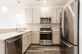 This single-floor unit at Whitty Road in Toms River, NJ offers a thoughtfully designed, open-concept layout finished with contemporary materials throughout. The main living area is spacious and bright, featuring wood-look plank flooring, recessed lighting, and a window that draws in natural light. A pendant-lit kitchen island anchors the transition between the living and kitchen spaces, providing both a functional workspace and a casual gathering spot.

The kitchen is well-appointed with cream shaker-style cabinetry, white quartz countertops, a subway tile backsplash, and a full suite of stainless steel appliances including a gas range, over-the-range microwave, and refrigerator. The open flow to the main living area makes the space feel connected and versatile.

A carpeted bedroom opens directly onto a private balcony through sliding glass doors, offering pleasant outdoor views and additional natural light. A ceiling fan adds comfort to the room. The full bathroom features floor-to-ceiling marble-look tile surrounding a soaking tub and shower combination, a white vanity with a clean-lined mirror, and coordinating marble tile flooring. A second bathroom presents light tile flooring and a streamlined vanity. Throughout, the unit maintains a clean, neutral palette that lends a fresh and move-in ready feel.