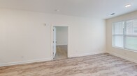 This single-floor, two-bedroom, one-bathroom unit offers a thoughtfully designed layout with generous overall square footage. The open-concept kitchen and living area serves as the heart of the home, where light-toned luxury vinyl plank flooring flows throughout. The kitchen is appointed with white shaker cabinetry, granite countertops, a subway tile backsplash, stainless steel appliances, and a peninsula with pendant lighting overhead — an ideal setup for both cooking and casual dining. The living area features multiple windows with horizontal blinds, allowing ample natural light and providing views of the landscaped exterior grounds.

The spacious primary bedroom features plush carpeting, a ceiling fan, a window with outdoor views, and direct access to a generously sized walk-in closet fitted with wire shelving. The second bedroom is equally well-sized with carpeted flooring and a closet. The full bathroom includes a white vanity with granite countertops, a framed mirror, modern light bar, and wood-look tile flooring. A dedicated laundry room houses a full-sized top-loading washer and dryer with overhead wire shelving for additional storage. A hallway connects the rooms efficiently, completing this well-organized and modern living space.