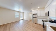 Located at 1385 W College Ave in Santa Rosa, CA, this single-floor unit offers a clean, modern design across three bedrooms and one bathroom. The open-concept kitchen and living area forms the heart of the home, featuring light hardwood-style flooring, recessed lighting, and a neutral white color palette that creates a bright, airy atmosphere. A door provides direct access to the exterior, allowing natural light to flow into the shared living space. The kitchen is well-appointed with white shaker-style cabinetry, light countertops, a stainless steel refrigerator, range, over-the-range microwave, and dishwasher, offering a full complement of modern appliances. The three bedrooms are finished consistently with the same light flooring and warm neutral walls, each featuring windows with blinds that provide natural light and privacy. The primary bedroom is a comfortable, well-proportioned space. The bathroom is finished with a white vanity, light countertop, a large mirror, a bathtub/shower combination, and matching hardwood-style flooring. The building exterior presents a contemporary multi-story facade with a clean, modern aesthetic and on-site parking, situated in a convenient Santa Rosa location.