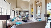 Located at 15270 Ballast Point Dr in Fort Myers, Florida, this single-story community clubhouse offers a generously proportioned, well-appointed gathering space designed to impress. The soaring double-height ceilings in the main lounge create a dramatic sense of openness, framed by large floor-to-ceiling windows that flood the interior with abundant natural light and offer views of the surrounding Florida landscape. Large-format tile flooring anchors the main areas, complemented by warm wood-tone flooring in the recreational zones.

The central lounge area features multiple seating arrangements with contemporary gray sofas and chairs accented by vibrant teal throw pillows, centered around stylish coffee tables. A bold yellow accent wall with vivid artwork and an elegant pendant light fixture adds a striking focal point. Adjacent to the lounge, a fully equipped leasing office area includes multiple workstations, patterned valances, and roller shades that filter the Florida sun.

A dedicated billiards room provides a lively entertainment option, complete with a full-size pool table beneath industrial-style pendant lighting, a coffered ceiling detail, and bar-height seating. A private lounge nook, outfitted with leather accent chairs, a wall-mounted television, and warm wood furnishings, offers a quieter retreat within the space.