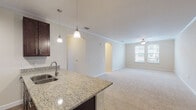 This single-floor residence offers a thoughtfully designed layout that balances open communal spaces with private quarters. The kitchen serves as a central hub, showcasing rich dark-espresso cabinetry reaching toward crown-molded ceilings, granite countertops, and a full suite of stainless steel appliances including a refrigerator, electric range, and built-in microwave. A peninsula with an undermount sink and pendant lighting above creates a natural boundary between the kitchen and the expansive living area, which features plush neutral carpeting, a ceiling fan, and arched architectural details that add visual interest to the open layout.

A carpeted hallway leads to the bedrooms, each finished with soft neutral carpet and windows that allow natural light to filter in. The primary bedroom connects directly to a private bathroom. Both bathrooms maintain a cohesive aesthetic, featuring wood-look flooring, dark vanity cabinetry with granite countertops, and tub-shower combinations tiled in large-format marble-style tile with decorative accent banding. Throughout the residence, crown molding, consistent hardware finishes, and a neutral color palette contribute to a polished, unified ambiance.