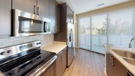 This single-floor residence showcases a contemporary design with a thoughtful, open layout. The kitchen serves as a central highlight, featuring dark espresso cabinetry that extends to the ceiling, a large quartz-topped island with an undermount sink, stainless steel appliances including a French door refrigerator and electric range, and a subway tile backsplash. Pendant lights and track lighting illuminate the space, which flows seamlessly into the living area. The living room features warm hardwood-style flooring, a ceiling fan, built-in shelving, and access to the outdoors through multiple large sliding glass doors and French doors that invite generous natural light and views of surrounding greenery. Carpeted bedrooms provide a comfortable retreat, each benefiting from outdoor access or large windows. The bathrooms include a full bath with a soaking tub and vertically stacked tile surround, a vanity bath with a walk-in closet featuring wire shelving, and a powder room with a pedestal sink, framed mirror, and light wood-look tile flooring. Warm neutral wall tones and white trim carry throughout, creating a cohesive and modern aesthetic.