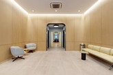 Located at 419 W 34th Street in Midtown Manhattan, this single-floor space offers a generous and well-appointed layout encompassing an entrance, multiple hallways, and a variety of rooms suited for collaborative and communal use. The entrance area sets a refined tone with warm wood-paneled walls, arched doorways, light stone-tiled flooring, and recessed lighting that creates a soft, welcoming ambiance. A dedicated mailroom features an extensive array of brass mailboxes beneath a sleek pendant light, complemented by clean white walls and matching stone tile. Throughout, arched transitions with dark-framed glass doors add architectural character while maintaining an open flow between zones. The main communal area is expansive and light-filled, featuring light hardwood floors, exposed coffered ceilings with integrated lighting, and a mix of modular lounge seating and bar-height tables with vibrant yellow accents. Several flexible meeting and gathering rooms branch off from this central space, each finished with white wainscoting, hardwood floors, and large multi-pane windows that invite generous natural light and views of surrounding greenery. A bright transition foyer features a glass-railed staircase with globe pendant lighting and an accessibility lift. The overall design blends classic architectural detailing with contemporary furnishings, creating a polished and functional environment.