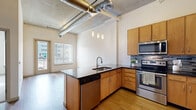 Located at 1545 Quitman St in Denver, CO, this single-floor urban loft-style unit blends industrial design with modern finishes throughout. The kitchen is a standout feature, showcasing warm wood cabinetry, dark granite countertops, a mosaic tile backsplash, and a full suite of stainless steel appliances including a refrigerator, range, microwave, and dishwasher. A peninsula with an integrated sink provides additional prep space and doubles as a casual dining area. Exposed metallic ductwork runs across the soaring ceilings, reinforcing the industrial-chic aesthetic that defines the space. Hardwood-style flooring flows through the main living areas, while plush carpet adds comfort to the bedroom spaces. The bedroom is generously proportioned, featuring a sliding barn door that opens to a closet, and benefits from abundant natural light streaming through large windows with blinds. An additional room with direct balcony access offers outdoor views of the surrounding neighborhood. The bathroom is well-appointed with a granite-topped vanity, warm wood cabinetry, and a tub-shower combination. Throughout, crisp white walls and natural light create a bright, airy atmosphere that complements the bold industrial elements of this Denver residence.
