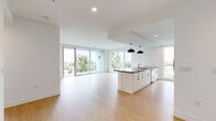 Located in San Diego's vibrant 92103 neighborhood, this contemporary 2-bedroom, 3-bathroom residence showcases a clean, modern aesthetic throughout. The open-concept living and dining area is anchored by light hardwood flooring and expansive floor-to-ceiling windows that flood the space with natural light while framing panoramic views of the surrounding cityscape. A central kitchen island with a dark countertop and sleek pendant lighting bridges the kitchen and living areas seamlessly. The kitchen itself is well-appointed with white cabinetry, a tile backsplash, and a full suite of stainless steel appliances. The generously sized primary bedroom features large windows with outdoor access to a private balcony, where a glass-railed terrace overlooks mature trees and the neighborhood below. The primary bath offers a modern vanity with a dark stone countertop, a barn-style door, and direct access to a spacious walk-in closet with built-in shelving. Additional bathrooms feature marble-style tiled tub surrounds and contemporary finishes. A second bedroom benefits from floor-to-ceiling windows with open city views. In-unit laundry adds everyday convenience. The overall ambiance is bright, airy, and polished throughout.
