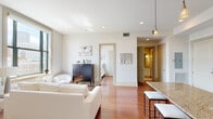 Located in New Orleans, this two-bedroom, two-bathroom unit offers a thoughtfully designed open-concept layout finished with rich hardwood flooring throughout the main living areas. The kitchen serves as a central hub, featuring warm cherry wood cabinetry, granite countertops, a substantial island with bar seating, pendant lighting, and a full suite of stainless steel appliances. A tray ceiling detail above the kitchen adds architectural interest and definition to the space.

The living area flows seamlessly from the kitchen, bathed in natural light from large windows that frame views of the surrounding New Orleans cityscape. Recessed lighting and pendant fixtures provide layered illumination throughout.

Both bedrooms are well-proportioned, each benefiting from large windows with city views and continued hardwood flooring. The two bathrooms are finished consistently with granite-topped white vanities, tile flooring, and pendant lighting with large mirrors. One bathroom includes a walk-in closet area, adding practical storage. The overall palette of neutral tones, clean white walls, and warm wood finishes creates a bright, cohesive, and inviting atmosphere throughout the unit.