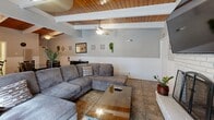 Located at 39900 Blacow Rd in Fremont, CA, this single-floor community space offers a well-appointed, open-concept layout that seamlessly combines a living room, dining area, and kitchen under one roof. The most striking architectural feature is the vaulted ceiling with exposed white-painted beams and warm wood paneling, which lends the space a welcoming, resort-like character. Multiple ceiling fans are installed throughout, ensuring comfortable airflow across the entire area.

The living room is anchored by a classic brick fireplace with a wall-mounted flat-screen TV above it, complemented by a large sectional sofa and a glass-top coffee table. Large sliding glass doors flood the space with natural light and provide direct views of and access to an outdoor pool and patio area. The kitchen features a white peninsula countertop with bar seating, stainless steel appliances including a full-size refrigerator and microwave, and decorative floating shelves with greenery. Adjacent to the kitchen, a dining area accommodates a full wooden table and chairs.

The space also includes two accessible bathrooms finished with classic tile wainscoting and grab bars, a utility room, a closet, and a connecting hallway. Tile flooring runs throughout, adding to the clean, functional aesthetic of this community gathering space.
