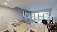 This well-appointed 2-bedroom, 1-bathroom unit is thoughtfully designed across a single floor, offering an efficient and comfortable layout. The open-plan kitchen and living area serves as the heart of the home, where a sleek kitchen features white cabinetry, stainless steel appliances including a french-door refrigerator and range, and a granite-topped peninsula with bar seating — ideal for casual dining or entertaining. Dark hardwood floors run throughout, adding warmth and contrast to the neutral grey and white color palette.

The living area is bright and airy, with large floor-to-ceiling sliding glass doors opening onto a private balcony that offers sweeping city skyline views. The primary bedroom is generously sized, featuring soft carpet, a built-in closet with shelving, and large windows that frame additional urban vistas. The second bedroom is equally well-lit, with wide windows showcasing a panoramic cityscape.

The bathroom is clean and functional, appointed with granite countertops, a large vanity mirror, and a shower-tub combination. A connecting hallway ties the layout together with ease. Recessed lighting throughout the unit ensures a consistently well-lit environment, while the modern finishes and open sightlines create a polished, contemporary ambiance suited to urban living.