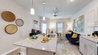 This thoughtfully designed one-bedroom, one-bathroom residence offers an efficient and comfortable layout across a single floor. The open-concept kitchen and living area forms the heart of the space, where light wood-style flooring, neutral gray walls, and generous natural light from multiple windows create a bright, welcoming atmosphere. The kitchen is equipped with stainless steel appliances, gray shaker-style cabinetry, a geometric tile backsplash, and a granite-topped island with pendant lighting overhead — ideal for both cooking and casual dining. A ceiling fan anchors the living area, which benefits from dual windows and direct access to a private patio overlooking a landscaped lawn.

The bedroom features plush carpeting, a window with natural light, and access to a dedicated walk-in closet outfitted with wire shelving. The bathroom includes a granite-topped vanity with gray cabinetry, a large mirror, overhead lighting, and wood-style flooring. The unit's exterior features stone and lap siding accents, contributing to its modern curb appeal.
