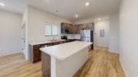 This two-story home is thoughtfully designed to maximize functionality across its two levels. The lower floor houses a spacious attached garage with a wide automatic door, offering ample room for vehicles and additional storage, alongside access to the main living areas above.

The upper floor serves as the primary living level and encompasses the majority of the home's total footprint. The open-concept kitchen is a standout feature, equipped with rich, dark-toned wood cabinetry, stainless steel appliances including a refrigerator, electric range, dishwasher, and microwave, all complemented by light marble-style countertops and a central island that provides additional prep and gathering space. Light hardwood-style flooring flows throughout the main living areas, enhancing the bright, clean aesthetic reinforced by recessed lighting and multiple windows with exterior views.

The living room benefits from natural light through dual windows and direct access to an outdoor balcony via a glass-panel door. The two bedrooms are carpeted and include ceiling fans, closets, and windows that bring in natural light. A shared full bathroom features wood cabinetry with marble-style countertops and hardwood-style flooring. A stacked washer and dryer unit is conveniently integrated into a dedicated laundry closet on the upper floor.