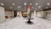 Located at 55 Elm St in Hartford, Connecticut, this generously proportioned single-floor amenity space offers a versatile and thoughtfully designed environment suited for both social gatherings and everyday use. The open-concept layout is anchored by light-toned large-format tile flooring that flows seamlessly throughout, creating a cohesive and airy atmosphere.

Exposed brick columns serve as striking architectural focal points, blending raw, industrial character with the space's contemporary aesthetic. A well-appointed wet bar with warm wood cabinetry, open shelving, and pendant lighting anchors one end of the space, complemented by bar seating and a dining area beneath a dramatic arrangement of pendant fixtures. Adjacent to this, a lounge nook with upholstered armchairs and a round accent table provides an intimate retreat.

Rich walnut wood-paneled walls define a distinct zone that transitions into a fitness area equipped with cardio machines, highlighted by dark exposed ceiling beams and track lighting. A welcoming lobby-style foyer features elevator access and a central pedestal table, establishing a polished entry point. Recessed lighting throughout ensures the entire space is evenly and warmly illuminated. Glass-paneled room dividers and multiple private access doors add functional flexibility to this refined, multi-use space.