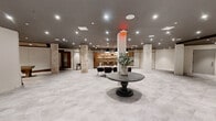 Located at 55 Elm St in Hartford, Connecticut, this generously proportioned single-floor amenity space offers a versatile and thoughtfully designed environment suited for both social gatherings and everyday use. The open-concept layout is anchored by light-toned large-format tile flooring that flows seamlessly throughout, creating a cohesive and airy atmosphere.

Exposed brick columns serve as striking architectural focal points, blending raw, industrial character with the space's contemporary aesthetic. A well-appointed wet bar with warm wood cabinetry, open shelving, and pendant lighting anchors one end of the space, complemented by bar seating and a dining area beneath a dramatic arrangement of pendant fixtures. Adjacent to this, a lounge nook with upholstered armchairs and a round accent table provides an intimate retreat.

Rich walnut wood-paneled walls define a distinct zone that transitions into a fitness area equipped with cardio machines, highlighted by dark exposed ceiling beams and track lighting. A welcoming lobby-style foyer features elevator access and a central pedestal table, establishing a polished entry point. Recessed lighting throughout ensures the entire space is evenly and warmly illuminated. Glass-paneled room dividers and multiple private access doors add functional flexibility to this refined, multi-use space.