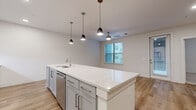 Located in Irving, TX, this well-appointed 2-bedroom, 1-bathroom residence offers a thoughtfully designed open-concept layout with modern finishes throughout. The combined kitchen and living area serves as the heart of the home, anchored by a large center island with a sleek quartz countertop, an undermount sink, and seating space. The kitchen is outfitted with crisp white shaker cabinetry, a subway tile backsplash, stainless steel appliances including a French door refrigerator, range, microwave, and dishwasher, and warm wood-look flooring. Stylish pendant lighting over the island adds a contemporary touch. The open living area features a ceiling fan, natural light from multiple windows, and direct access to an outdoor area via a glass-paneled door. Both bedrooms are carpeted and include ceiling fans and windows that invite natural light. The primary bedroom connects to a spacious walk-in closet with built-in shelving and hanging rods for ample storage. The bathroom is elegantly finished with marble-style tile surrounding a soaking tub and shower, a white vanity with an undermount sink, wood-look flooring, and brushed nickel fixtures. A connecting hallway with wood flooring ties the rooms together seamlessly.