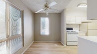 This single-floor residence offers a clean, functional layout designed for comfortable everyday living. Light hardwood flooring runs consistently throughout the space, creating a cohesive and easy-to-maintain interior. Neutral warm-taupe walls complement the bright, airy feel found in each room.

The living area is generously sized, filled with natural light from a window overlooking the surrounding neighborhood. A ceiling fan with a built-in light fixture adds both practicality and airflow to the space. Textured ceilings are present throughout, adding a subtle tactile detail to each room.

The galley-style kitchen is efficiently organized, featuring white cabinetry on both sides, a stainless steel sink, white appliances including a range and refrigerator, and ample countertop space. The layout maximizes storage and workflow within a compact footprint.

Multiple bedrooms are accessible via a central hallway, each offering generous floor space, neutral walls, and closet storage. Natural light filters into the bedrooms through windows with blinds. A bathroom with white cabinetry and a vanity is conveniently located along the hallway.

Overall, the space presents a practical and well-maintained interior with a consistent design language—light floors, neutral tones, and functional features—that creates a welcoming and adaptable environment.