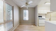 This single-floor residence offers a clean, functional layout designed for comfortable everyday living. Light hardwood flooring runs consistently throughout the space, creating a cohesive and easy-to-maintain interior. Neutral warm-taupe walls complement the bright, airy feel found in each room.

The living area is generously sized, filled with natural light from a window overlooking the surrounding neighborhood. A ceiling fan with a built-in light fixture adds both practicality and airflow to the space. Textured ceilings are present throughout, adding a subtle tactile detail to each room.

The galley-style kitchen is efficiently organized, featuring white cabinetry on both sides, a stainless steel sink, white appliances including a range and refrigerator, and ample countertop space. The layout maximizes storage and workflow within a compact footprint.

Multiple bedrooms are accessible via a central hallway, each offering generous floor space, neutral walls, and closet storage. Natural light filters into the bedrooms through windows with blinds. A bathroom with white cabinetry and a vanity is conveniently located along the hallway.

Overall, the space presents a practical and well-maintained interior with a consistent design language—light floors, neutral tones, and functional features—that creates a welcoming and adaptable environment.