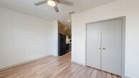 Located at 325 Duval St E in Jacksonville, FL, this efficiently designed single-floor unit makes excellent use of its compact footprint. Warm-toned hardwood-style flooring runs throughout, lending a cohesive and modern aesthetic to the entire space. The open-concept main living area is bright and airy, featuring a ceiling fan and a window with slatted blinds that allows natural light to fill the room. A double-door closet provides convenient storage directly within the living area. The galley-style kitchen is thoughtfully outfitted with dark cabinetry, light countertops, and a full suite of black appliances including a refrigerator, stove, dishwasher, and built-in microwave. A hallway connects the kitchen to the rest of the unit, leading to a dedicated laundry closet with a stacked washer and dryer. The bathroom features hardwood-style flooring, a combination tub and shower, a toilet, and a vanity with dark wood cabinetry and a white countertop, all presented in a clean, neutral palette. Recessed lighting and a consistent use of white walls contribute to a bright, contemporary ambiance throughout the unit.