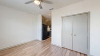 Located at 325 Duval St E in Jacksonville, FL, this efficiently designed single-floor unit makes excellent use of its compact footprint. Warm-toned hardwood-style flooring runs throughout, lending a cohesive and modern aesthetic to the entire space. The open-concept main living area is bright and airy, featuring a ceiling fan and a window with slatted blinds that allows natural light to fill the room. A double-door closet provides convenient storage directly within the living area. The galley-style kitchen is thoughtfully outfitted with dark cabinetry, light countertops, and a full suite of black appliances including a refrigerator, stove, dishwasher, and built-in microwave. A hallway connects the kitchen to the rest of the unit, leading to a dedicated laundry closet with a stacked washer and dryer. The bathroom features hardwood-style flooring, a combination tub and shower, a toilet, and a vanity with dark wood cabinetry and a white countertop, all presented in a clean, neutral palette. Recessed lighting and a consistent use of white walls contribute to a bright, contemporary ambiance throughout the unit.
