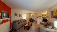 This single-floor residence is thoughtfully designed to maximize both comfort and functionality. The open-concept living and dining area serves as the heart of the home, where a bold terracotta accent wall with a decorative shelf creates a striking focal point. Wood-style flooring anchors the living space, transitioning to carpet in the seating area, while natural light flows in through large windows. A ceiling fan with a light fixture illuminates the adjacent dining area, which connects seamlessly to the kitchen via a pass-through counter. The kitchen is well-equipped with warm oak cabinetry, ample counter space, a double sink, and black appliances including a range and refrigerator, all set on durable wood-look flooring. The primary bedroom offers a cozy, carpeted retreat with generous space for furnishings, while the second bedroom provides direct access to one of the two full bathrooms. Both bathrooms feature wood-tone vanity cabinetry, stone-look countertops, and wood-style flooring. The layout, as visible in the dollhouse view, offers a practical and connected flow between all rooms, making this a comfortable and well-organized living space.